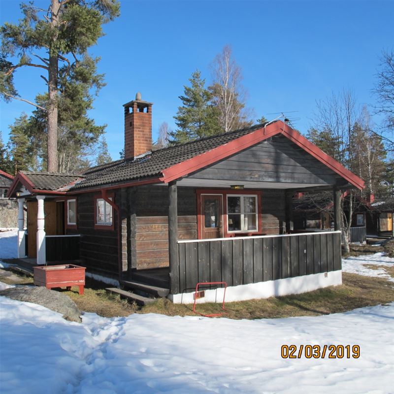 A grey cottage with red linings and snow-covered lawn.