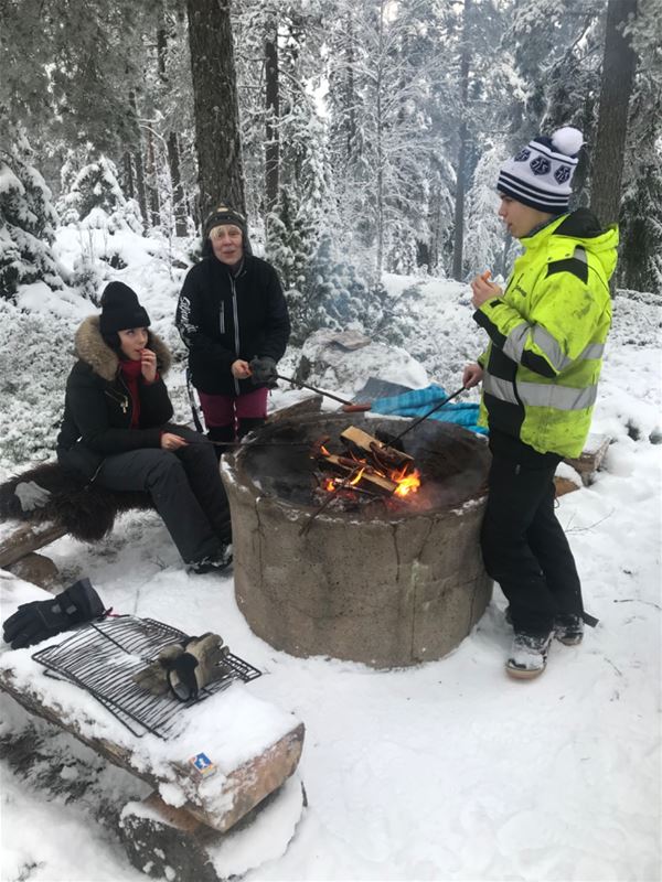 Några personer grillar vid en grillplats en vinterdag. 