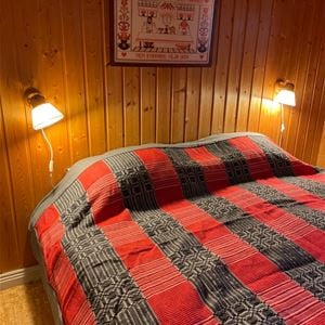 Double bed with grey and red bedspread against a pine wall. 