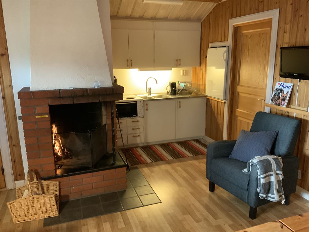 Open fire place beside the kitchen and an armchair in front of the fire. 