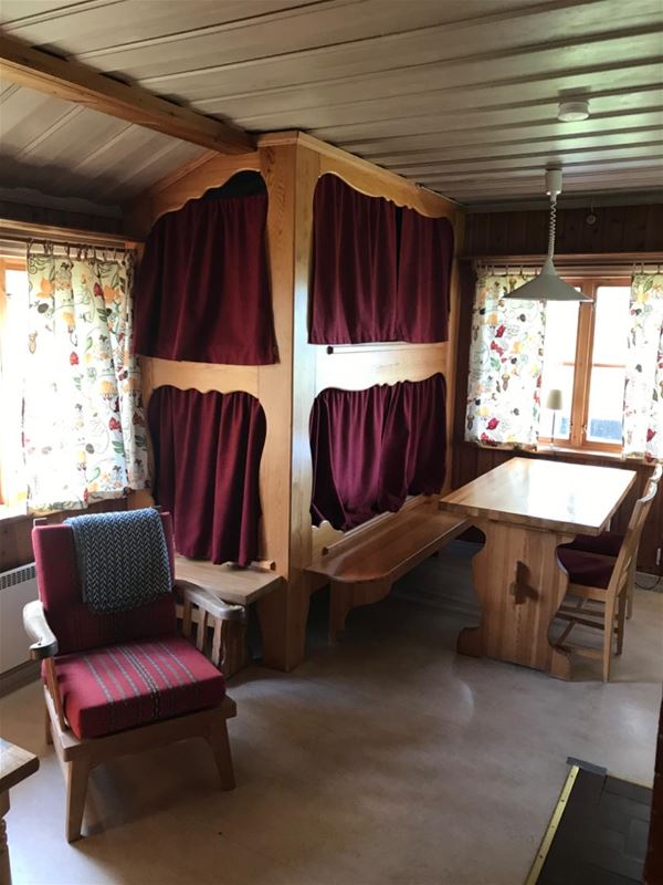 Site-built bunk bed with red curtains with wooden dining furniture and a red armchair.