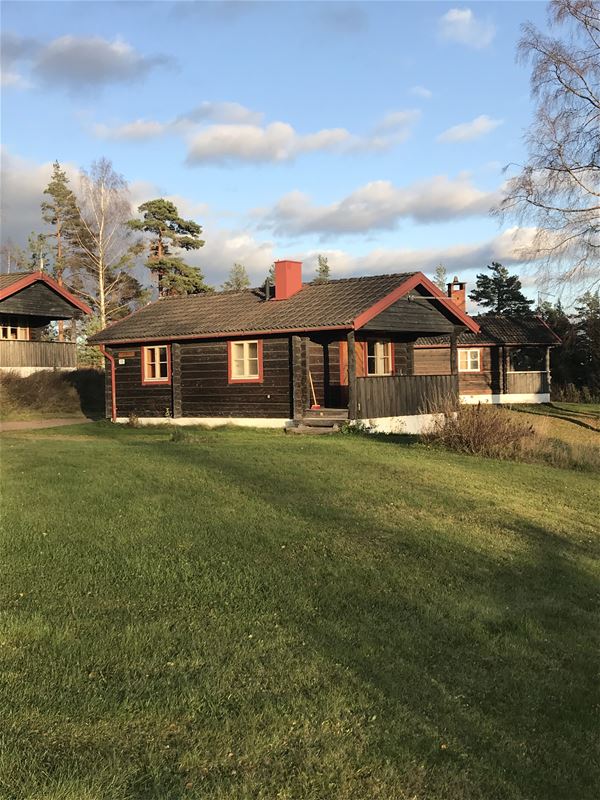 Grey timber cottage with red linings an a terrace with roof. 