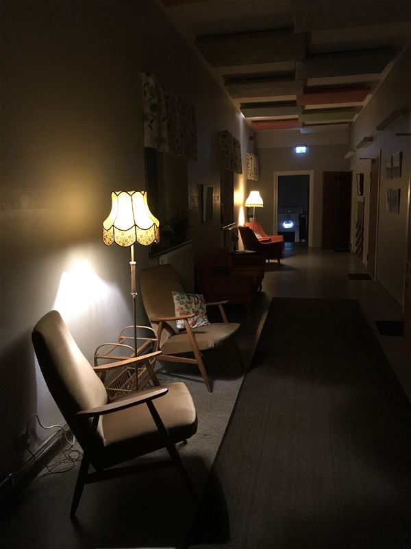 Two armchairs in a dark hall lighted by a lamp on the floor.. 