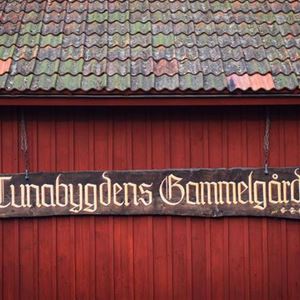 Ett rött gammalt trähus med en målad skylt för Tunabygdens Gammelgård.