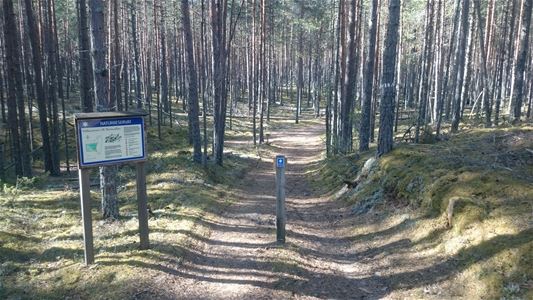 Sign with information and deciduous forest around a path in the middle.