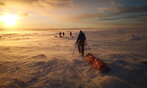 Några personer åker skidor på kalfjället i soluppgång.