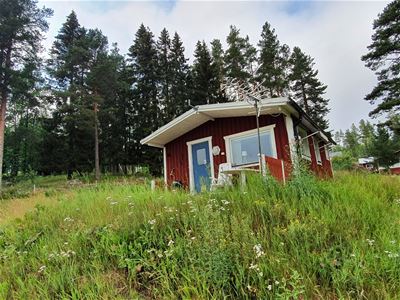 Färgbild - exteriör rödvit stuga med natur i bakgrunden.