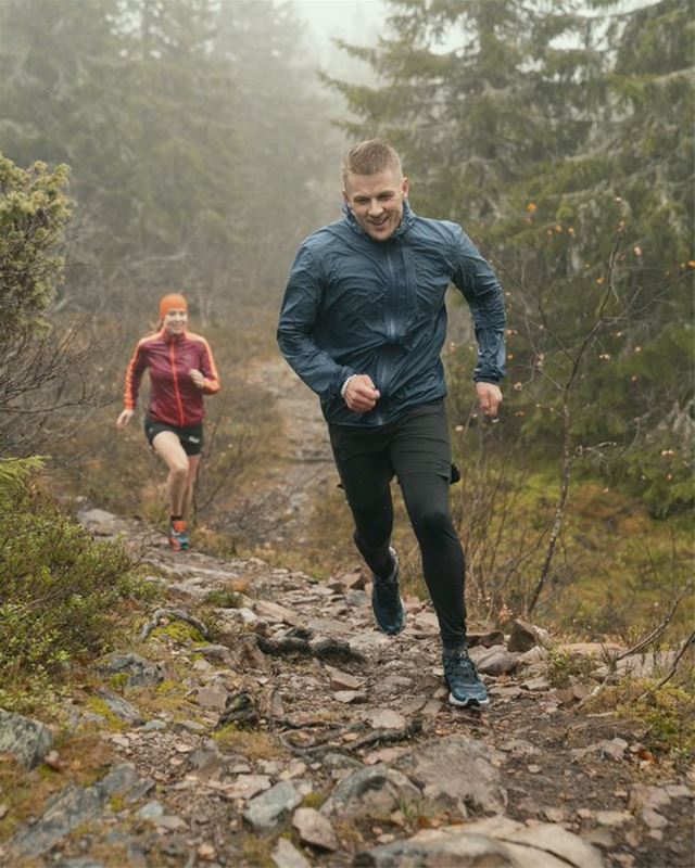 A man and a woman run towards the camera on a rocky path in fog.