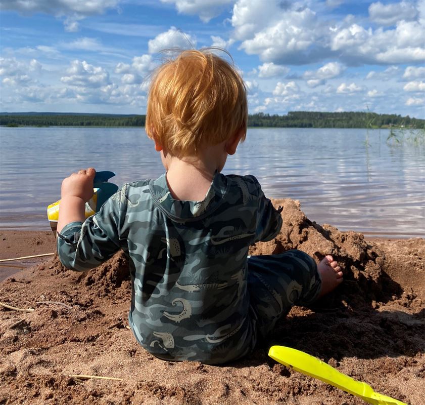 Liten pojke bygger sandslott på stranden i vattenbrynet.