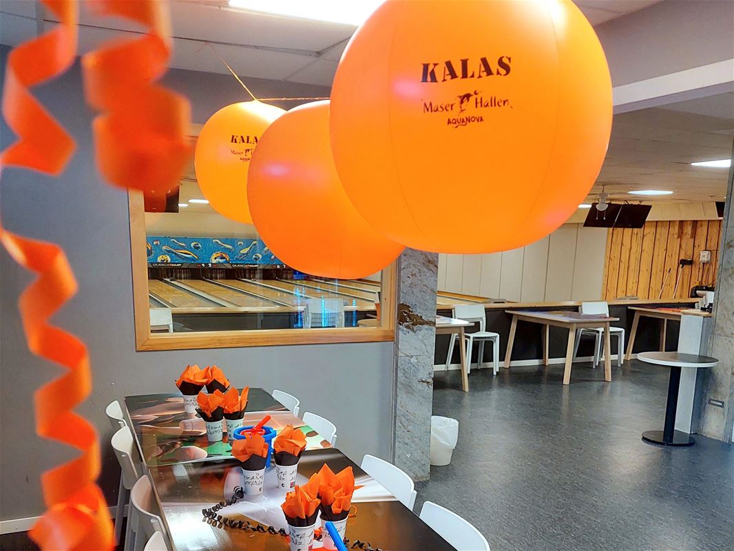 Ett bord dukat med oranga servetter och med balonger som hänger ovanför bordet.