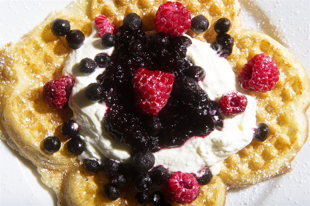 A waffle with jam, cream and berries. 