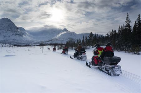 seks snøscootere på tur med snødekte fjell i bakgrunnen
