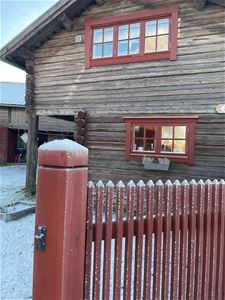 Grey timbercottage with red windows and a red fence. 