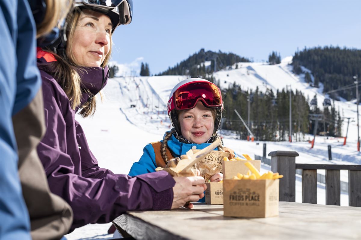 A family sits and eats near the ski slope.