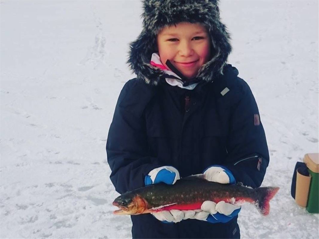 En vinterklädd liten pojke som håller i en fisk.