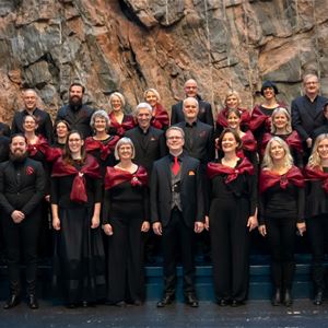 Foto: Mattias Henningsson,  © Mattias Henningson, En grupp män och kvinnor i svarta kläder, kvinnorna ,med röda sjalar över axlarna, en julgran  och en bergvägg i bakgrunden.