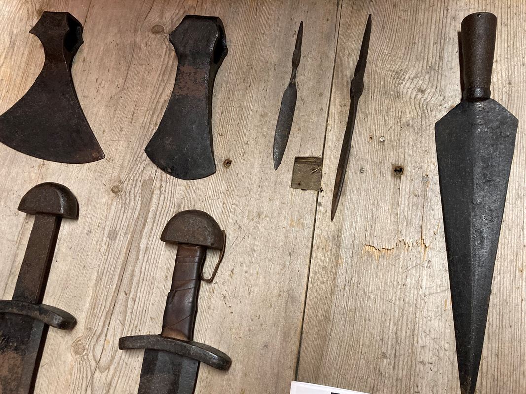Iron objects such as ax blades and spearheads lie on a table.