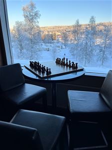 A chess in silhouette in front of a window with a view of frost covered trees. 
