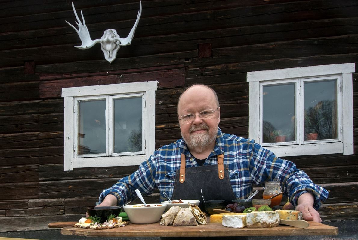 Kalle Moraeus står utomhus och håller en bricka med ostar och tillbehör. 