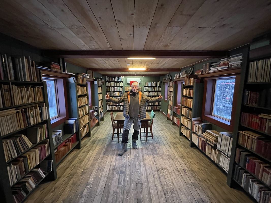 En man står i ett bibliotek med bäcker längs väggarna och under fönstren. 