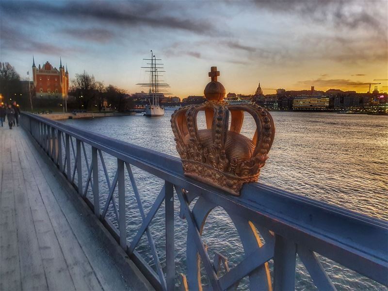 Kunglig krona på broräcke med Skeppsholmen i bakgrunden 