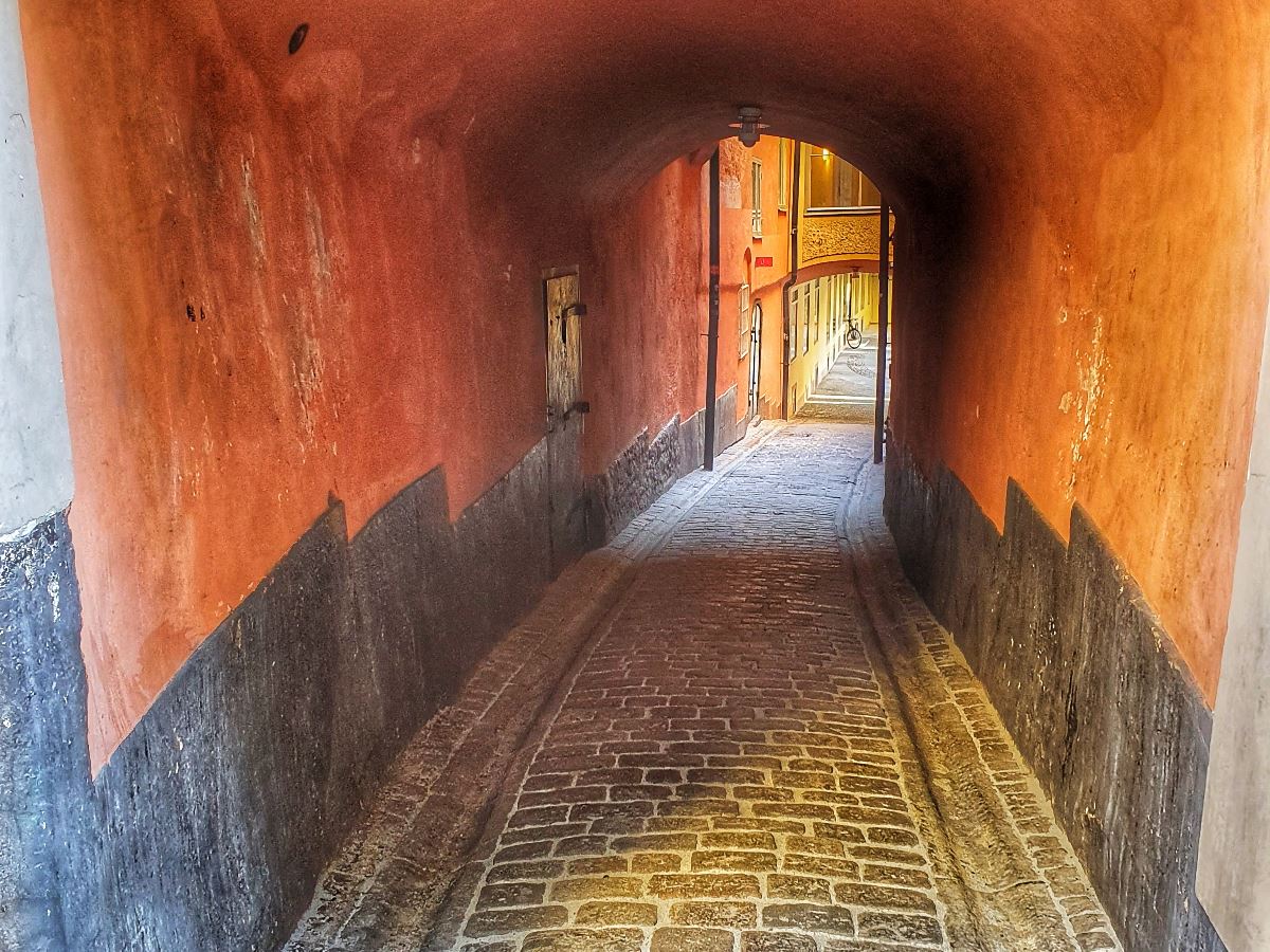 En smal tunnel genom gammal byggnad och gata av klappersten