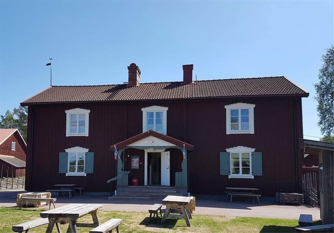 Slöjdstugan på Rots Skans, röd timrad byggnad med bord på gräsmattan.