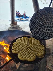 A baked waffle in a waffle iron over an open fire.
