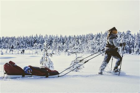 Woman in snowshoes pulling a sled in the snow.