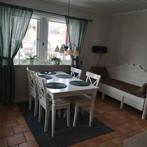Matbord med fyra stolar framför ett fönster och en vitmålad kökssoffa. 