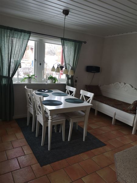 Matbord med fyra stolar framför ett fönster och en vitmålad kökssoffa.  
