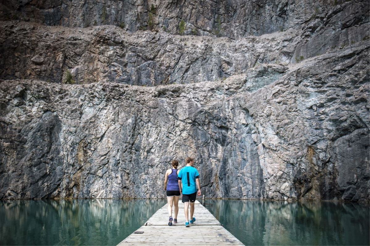 Ett par som går ut på bryggan ut mot det gröna vattnet och klippväggen.