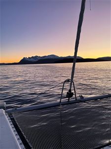 Båt ut i fjorden med fine fjell og solnedgang i bakgrunnen