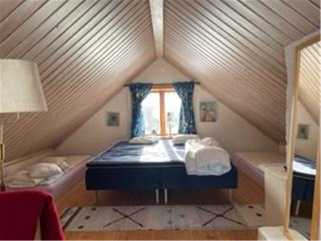 Double bed under the window on a loft with sloping ceiling. 