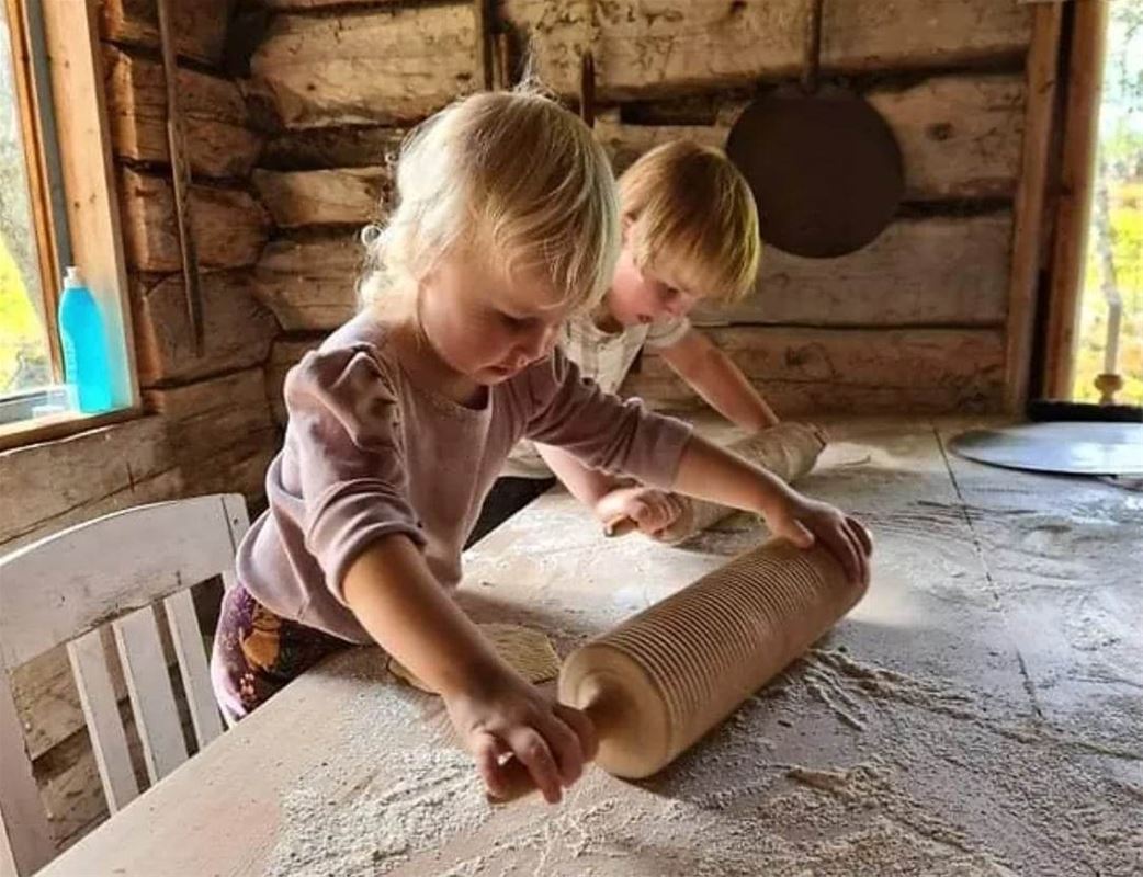 Två barn står vid ett bord med varsin kavel och kavlar ut tunnbröd.