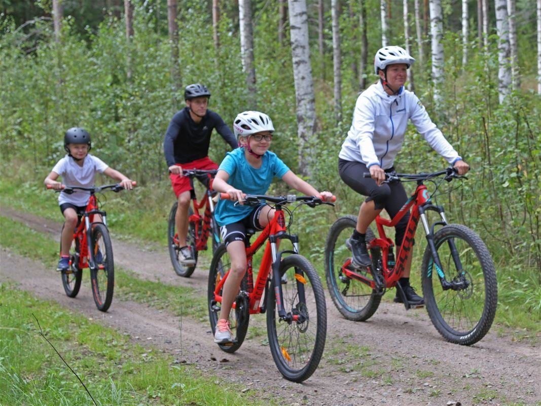 En man och en kvinna och två barn som cyklar på en grusväg på var sin röd cykel.