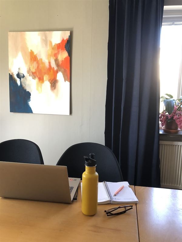 A table with laptop, pen, paper, glasses and a bottle of water. 