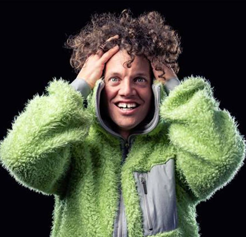 Ett porträttfoto på Nassim i grön jacka och som håller sina händer i sitt lockiga hår. Han ser in i kameran och ser busig ut.