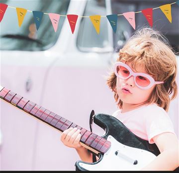 Ett barn i rosa solglasögon, rosa t-shirt och en elgitarr i handen. Barnet ser cool ut. 