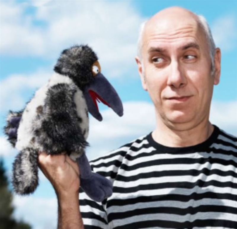 Bild på "Kråkan" som är en man i svarvit-randig tröja och håller en gosedjurs-kråka i handen som han tittar på.