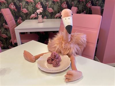 Interiör bild, färgbild - en rosa pelikan sittande på ett bord med fikabröd på en tallrik