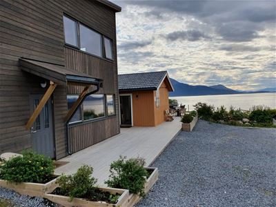 Wooden house by the water with mountains in the background and a garden in front