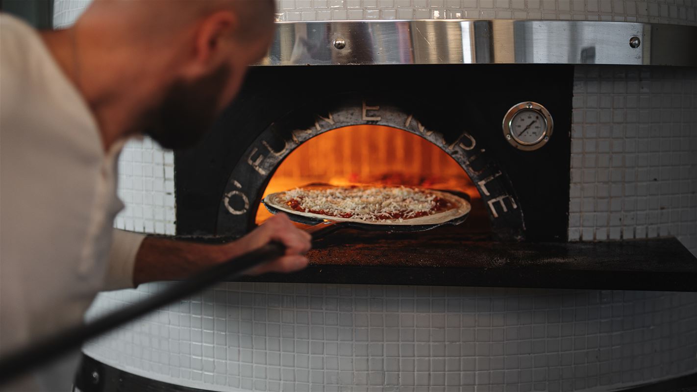 Anders stoppar in nygjord pizza i den speciella ugnen med mycket hög värme.