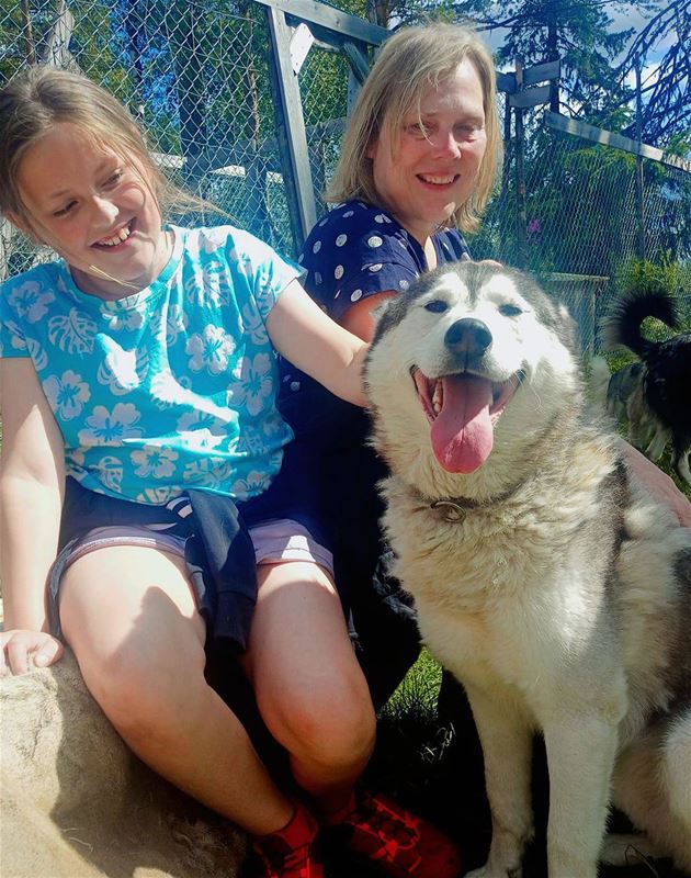 Two people sit next to a husky dog.