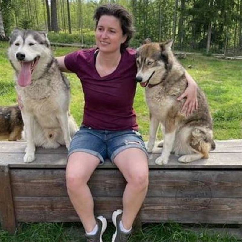 A lady sits in the middle between two husky dogs.