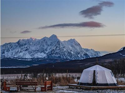 Snow-covered mountains with a white tent and benches in the foreground under a clear sky.