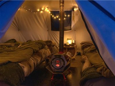 Inside a tent with two beds, a wood-burning stove, and string lights.