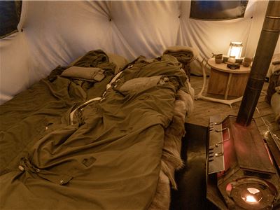 Cosy tent interior with sleeping bags, a wood-burning stove, and soft lighting.