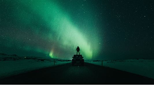 Mann som står på en bil og ser på nordlys