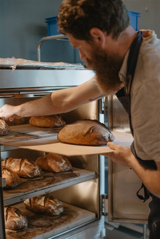 Bagare med nybakat bröd på plåtar.